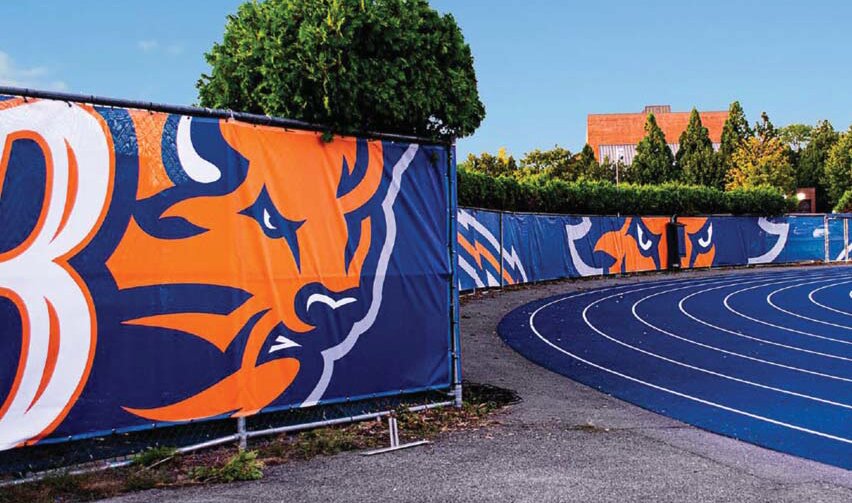 Custom mesh fence banners with team mascot art around an athletic track